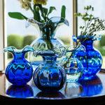 A set of cobalt blue and clear glass flower vases arranged on a dark wooden table in front of a bright window.