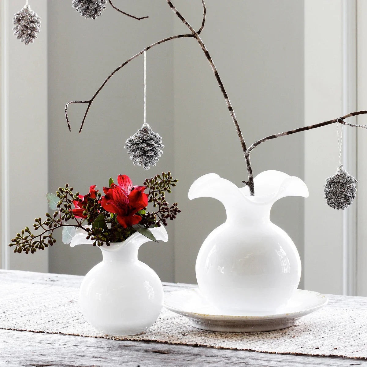 Two white vases with decorative flowers and branches on a wooden surface.