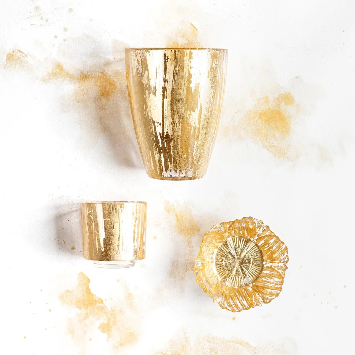 Two gold tumblers and a decorative gold plate on a white background with marble-like texture.