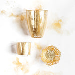 Two gold tumblers and a decorative gold plate on a white background with marble-like texture.